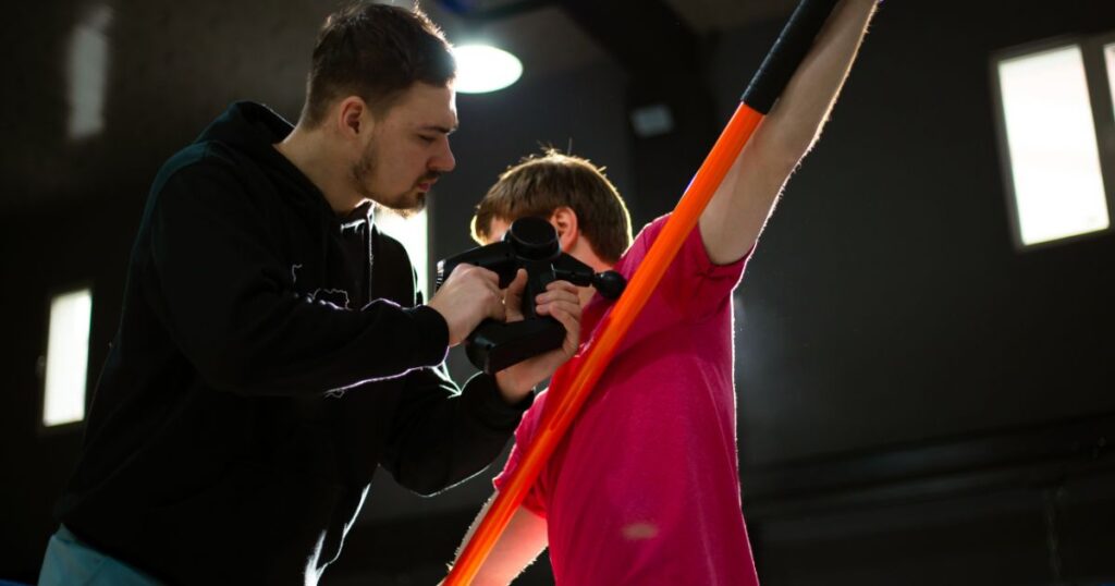 A physical therapist using a massage gun on a young athlete.